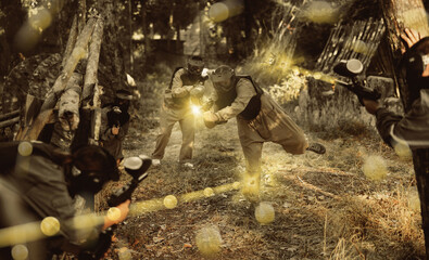 Team eliminating opponents on paintball field. People in protective outwear and helmets aiming with paintball markers.