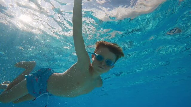 Cheeky 7 year old boy swims underwater with cheeks puffed, puts hand over camera