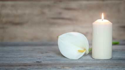CALLA FLOWER AND A LIGHTED CANDLE ON WOOD BACKGROUND. DECEASE, FUNERAL AND MEMORIAM. COPY SPACE.	