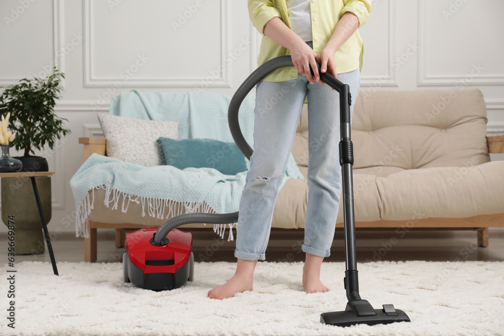 Wall mural Woman cleaning carpet with vacuum cleaner at home, closeup