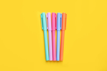 Many colorful markers on yellow background, flat lay