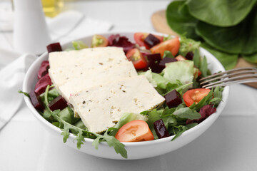 Bowl of tasty salad with tofu and vegetables on white tiled table, closeup