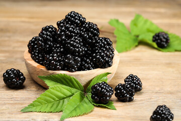 Ripe blackberries and green leaves on wooden table, closeup
