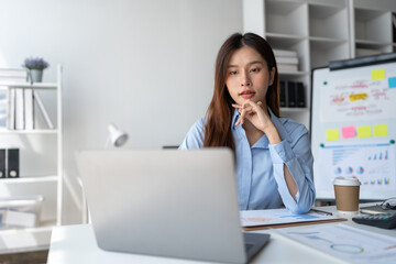 Asian businesswoman sitting and thinking analyze financial reports Business growth using laptop computer and documents, graphs, charts, investment calculators. Office business plan