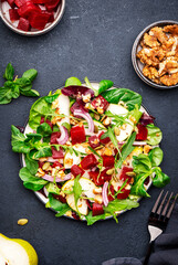 Gourmet salad with beetroot, pear, arugula, lettuce, red onion, chard and walnut, black kitchen table. Fresh delicious dish for healthy eating