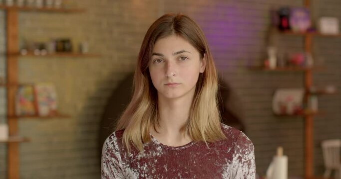 Young female tired student close portrait experiencing neutral serious mood, reflecting her current emotions. Individual not to smile for photos, introspective look. Serious expression of young adult.