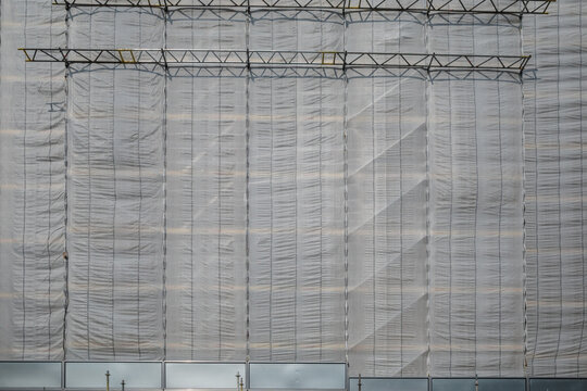 Front exterior view of net wrap scaffolding in front of building at construction site.