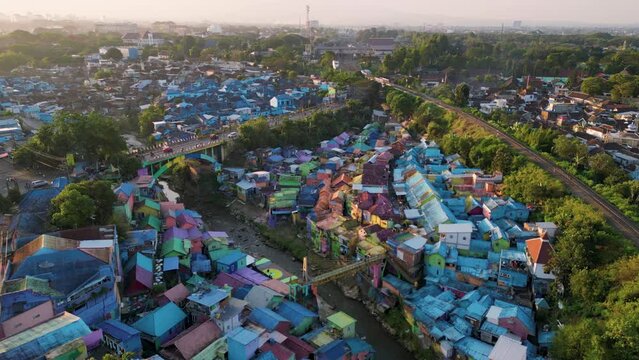 Bird eye view of Jodipan Village aka Rainbow Village with a train line passing next to it and a bridge with cars passing on it - sunset time in Malang, East Java - Indonesia