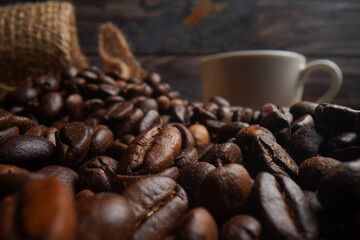 Coffee beans in a red coffee cup and many coffee beans placed around on a wooden table in a warm, light atmosphere, on a dark background, with copy space.