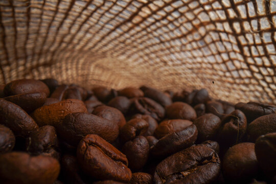 The picture of many coffee beans placed around in a sack of coffee in a warm light atmosphere.