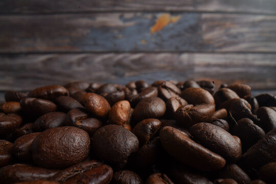 Close up, The picture of coffee beans stacked together on a wooden floor in a warm, light atmosphere, on dark background, with copy space.