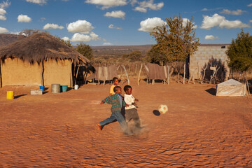 village african kids playing soccer on an improvised football field in the yard between the...