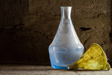 Antique dishes on a dusty wooden shelf. An old dirty bottle and funnel. An old glass bottle in a...