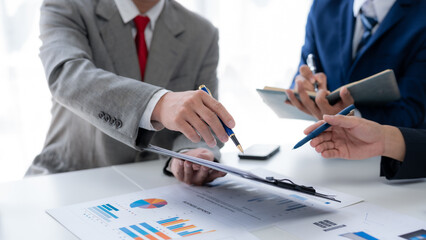Business people together in a meeting using pen pointing at financial data graph in office.