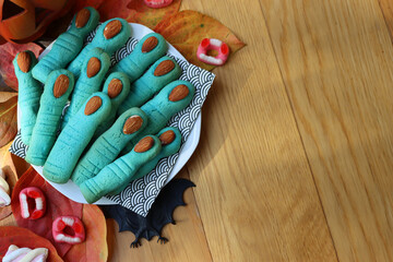 Blue Witch’s fingers cookies for Halloween on a plate on wooden table with decorations and candies