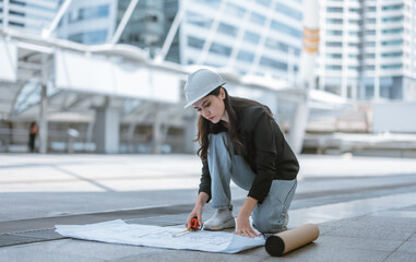 Expert female architect reviews Skytrain site, cross referencing blueprint for project approval.