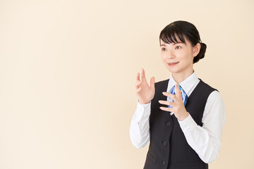 説明するベストにリボンタイの制服を着た、受付業務、事務業務の女性