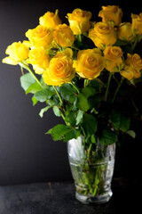bouquet of beautiful yellow roses with leaves in a vintage crystal vase on a black background