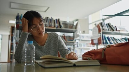 Asian girl with hand on head feeling tired and stressed while read books and take medicine in library at university.