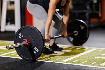 Fototapeta na wymiar Close up of a fit female bodybuilder lifting heavy barbell in a gym.