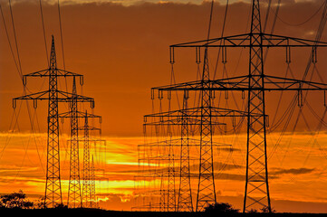 Strommasten und Überlandleitungen vor stimmungsvollem Abendhimmel im Gegenlicht des Nachglühens der untergegangenen Sonne am Horizont