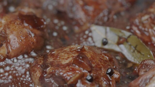 filipino adobo chicken thighs and chicken legs simmering in dark glaze sauce.