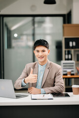 Young handsome man typing on tablet and laptop while sitting at the working wooden table modern office room..