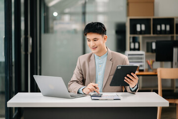 Fototapeta premium Business asian man Talking on the phone and using a laptop with a smile while sitting at modern office