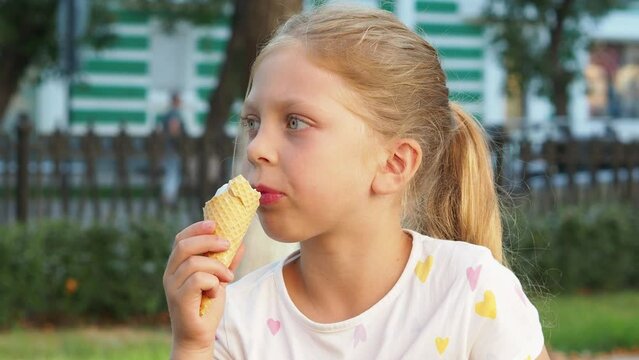 happy girl eats ice cream in a waffle cone on the street, a child in a t-shirt has a snack in the park in summer. Delicious sweet food. Large cold ice cream in a waffle cone. Natural ice cream