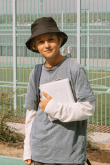 boy holding copybooks standing at school playground, smiling and looking at camera