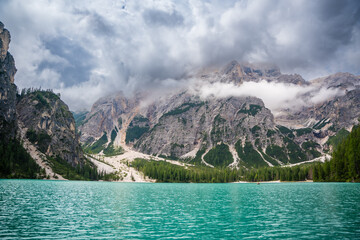 Braies lake surrounded by pine forests and the rocky ranges of the Dolomites in cloudy day, Italy.