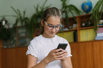 cute smiling teenage girl posing with smartphone at classroom