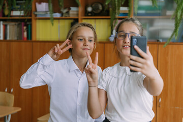 cute smiling teenage girl and boy posing with smartphone at classroom