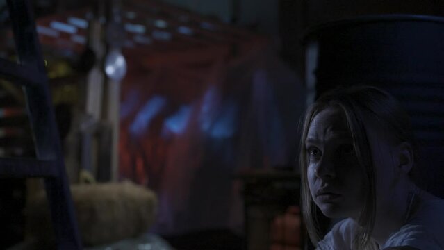 Scared blonde girl, victim of the horror maniac hiding from the man behind the barrel in the warehouse. HDR BT2020 HLG Material.