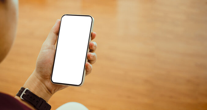Mockup image of asian man holding black smartphone with blank white screen at home.