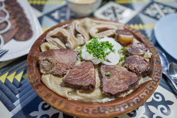 traditional Kazakh Asian dish Beshbarmak: noodles with lamb and onions close-up on a plate on the table. near the broth in bowls. dastarkhan. bolied beef and horse meat
