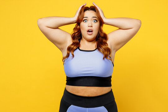 Young Shocked Frightened Chubby Overweight Plus Size Big Fat Fit Woman Wear Blue Top Warm Up Training Hold Head Look Camera Isolated On Plain Yellow Background Studio Home Gym. Workout Sport Concept.