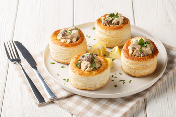 Vol-au-Vent is a hollow puff pastry shell filled with a creamy mushroom and chicken filling closeup on the plate on the white wooden table. Horizontal