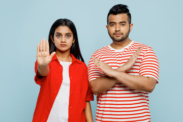 Young couple two friends family Indian man woman wear red casual clothes t-shirts together showing stop gesture with palm, holding hands folded crossed isolated on plain light blue color background.