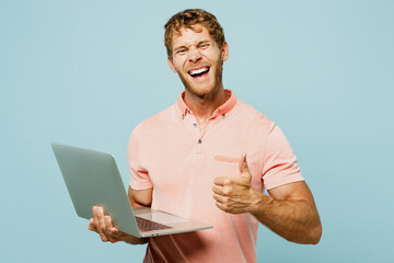 Young satisfied blond IT man wear pink t-shirt casual clothes hold use work on laptop pc computer...