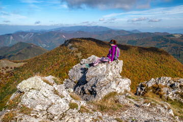 Woman hiker sitting on th rock on top of the hill Klak and looking on beautiful mountain landscape under