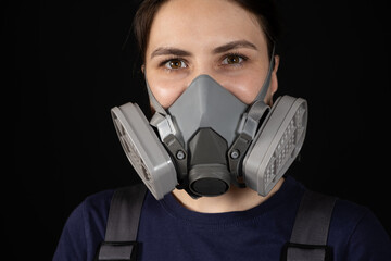 A woman wears a protective respirator with dust and gas filters on a black background.