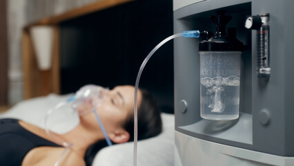 Portrait of a sick young woman who uses an oxygen concentrator and an inhaler for treatment at...