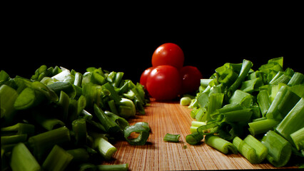 Cutting, cooking process, tasty and bright image, green onion with a bright tomato, on a dark background.