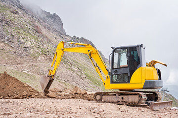 Excavator works in the highlands. Makes a trench for communications. water and electricity. in the gorge of the mountains. repair and expansion of a road