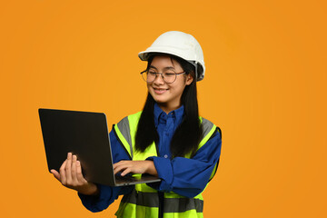 Smiling Asian girl wearing helmet holding laptop isolated on yellow background, future dream job career as engineer and architect