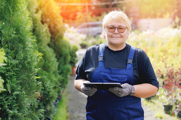 Senior gardener woman using tablet computer for garden shop control inventory flowers and plants....