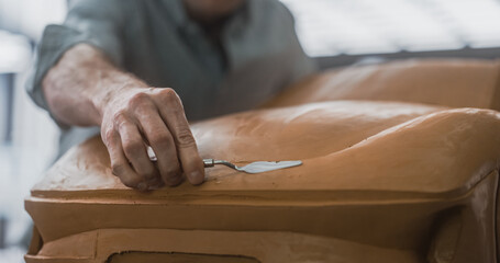 Close Up of an Automotive Designer Sculpting a 3D Clay Model of a New Production Car. Professional Modeler Using a Spatula to Carefully Smooth Out the Surface of a Prototype Sustainable Vehicle