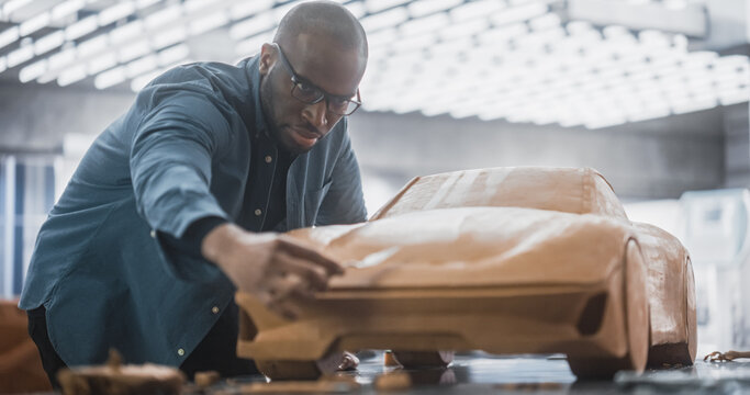 Portrait of a Handsome Automotive Designer Developing a 3D Clay Model of a New Production Car. Professional Black Man Using Spatula to Smooth Out and Trim the Surface of a Prototype Concept Car - Powered by Adobe