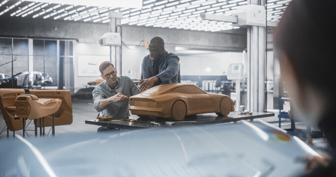 Team of Automotive Designers, Modelers and Engineers Working on Creating a Futuristic Car in a Studio. Female Drawing a Vehicle Sketch on Digital Tablet, Two Designers Work on a Clay Model